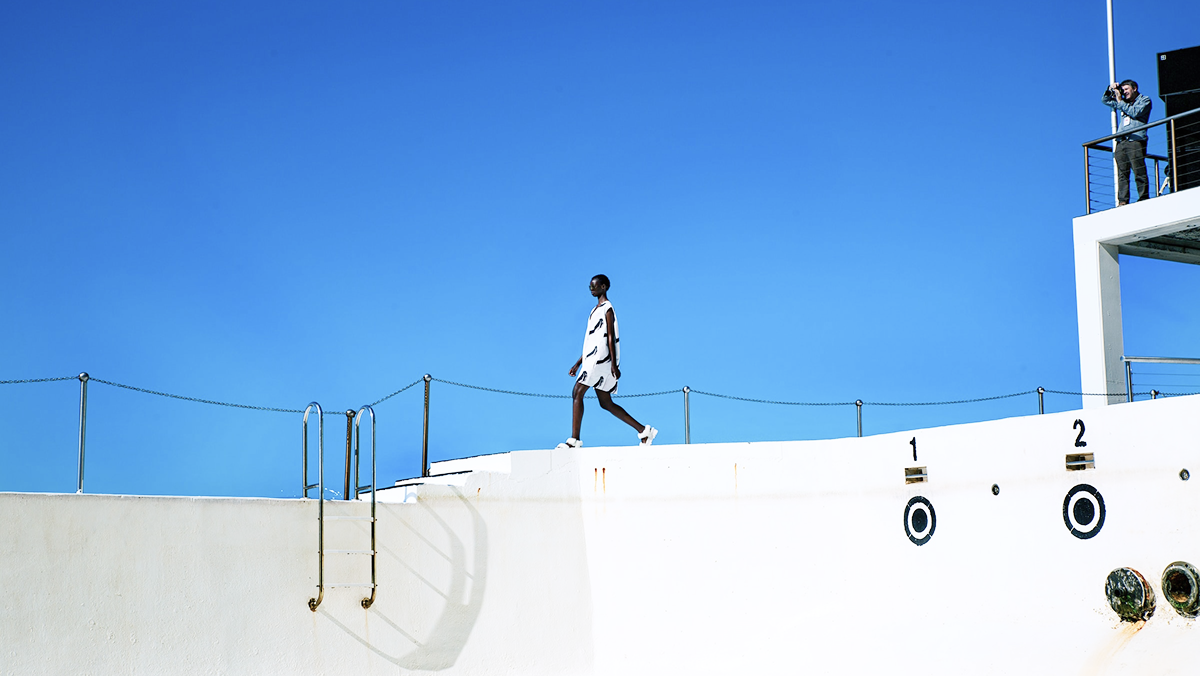 A lone figure walking a white rooftop terrace against a deep blue sky