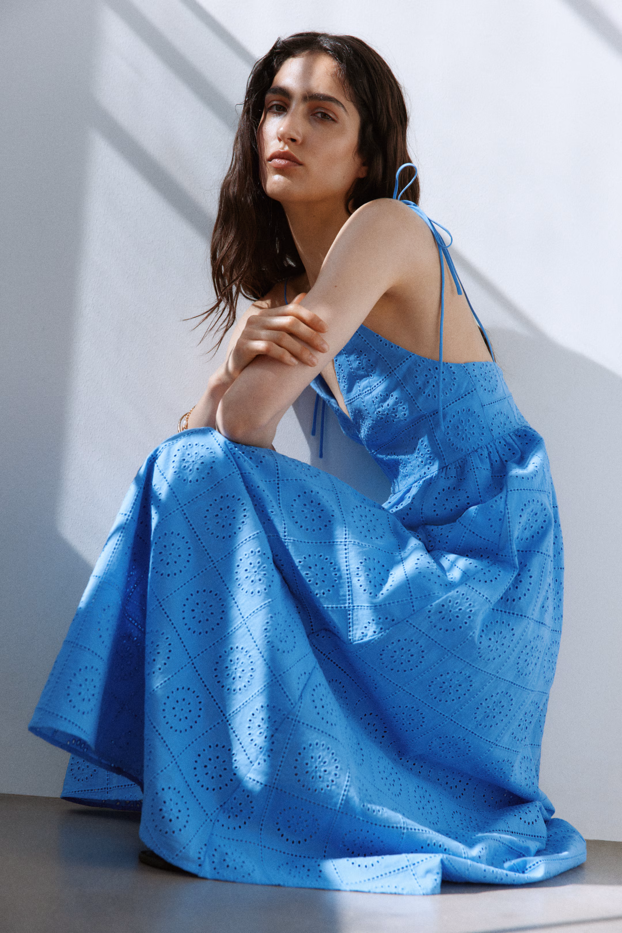 Model seated in a blue broderie-anglaise eyelet maxi dress