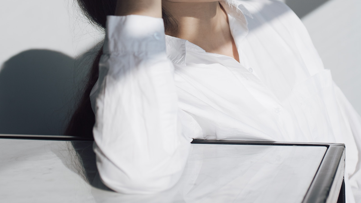 Model resting against a steel table in a soft white shirt, bathed in daylight